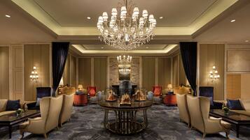 Um hall de hotel luxuoso com um lustre imponente, assentos confortáveis e uma parede de detalhes em mármore.