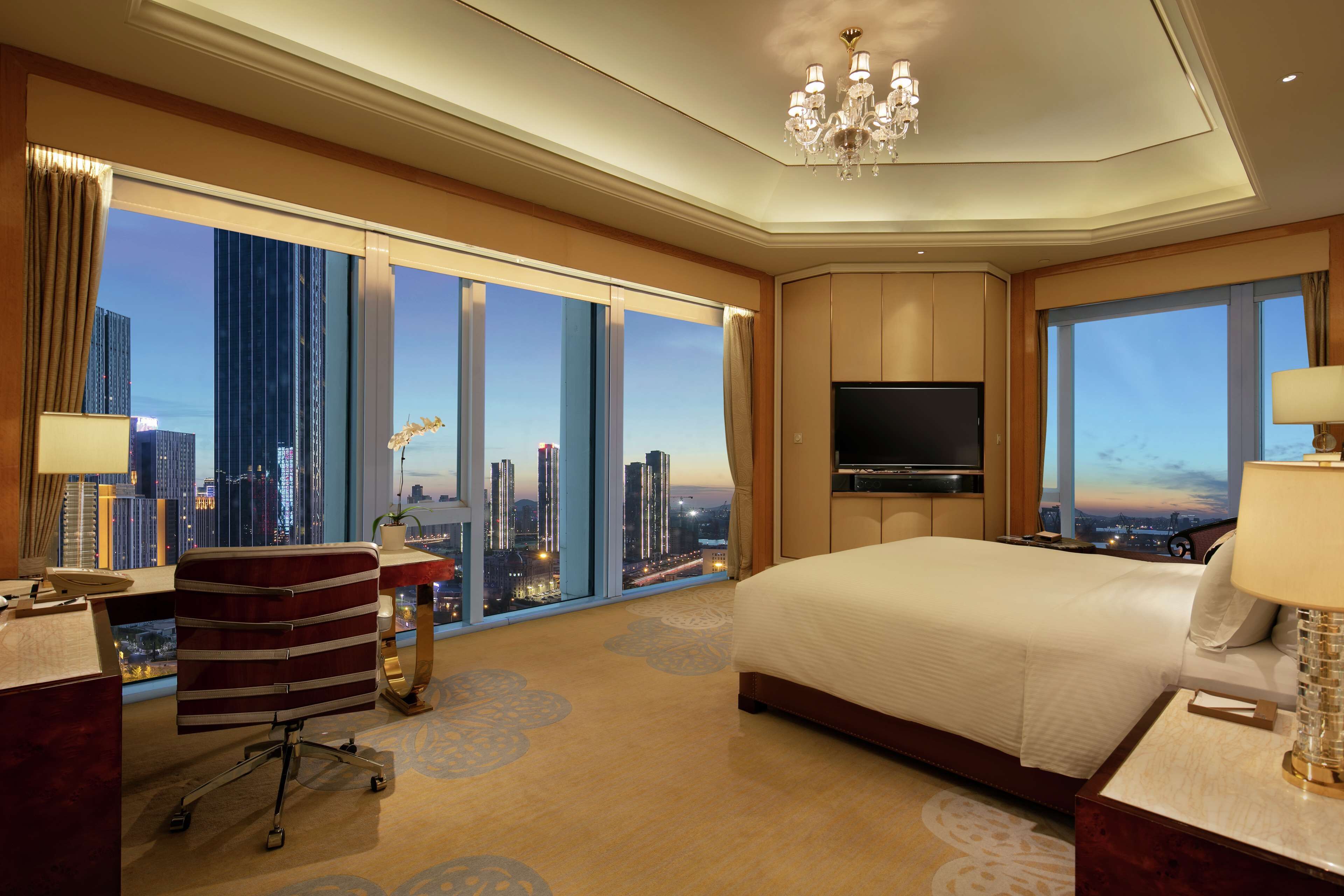 Habitación de hotel con una cama grande, un escritorio con silla, un televisor y vistas a la ciudad.