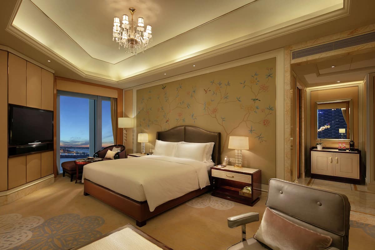 Ein geräumiges Hotelzimmer mit einem großen Bett, einem Fernseher, einem Schreibtisch und Blick auf die Stadt.