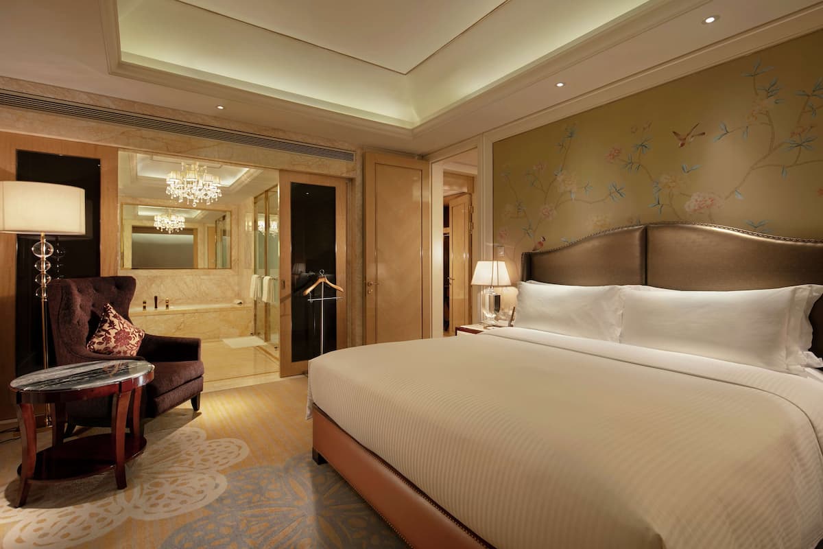 Ein geräumiges Hotelzimmer mit einem großen Bett, einer Sitzecke mit Sessel und Tisch, einem Badezimmer mit Badewanne und einer Wand mit floralem Dekor.
