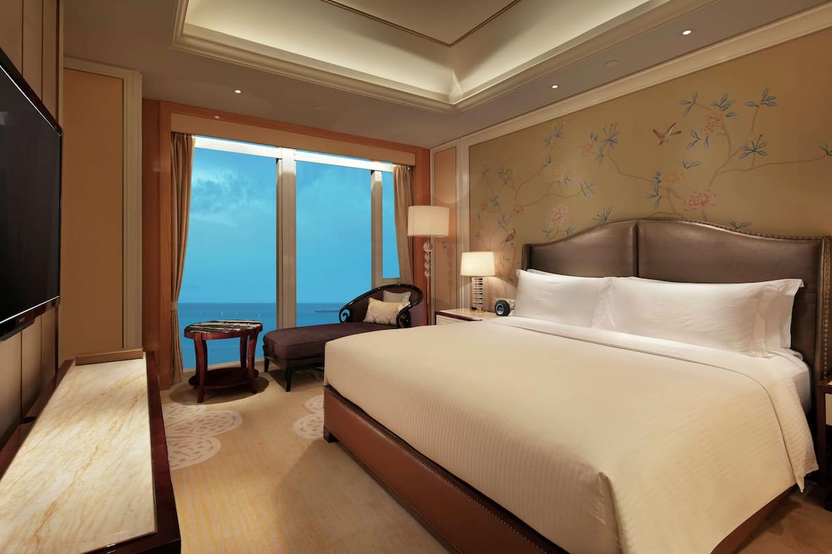 Ein Hotelzimmer mit einem großen Bett, einem Schreibtisch, einem Stuhl, einem Fernseher und Blick aufs Meer.