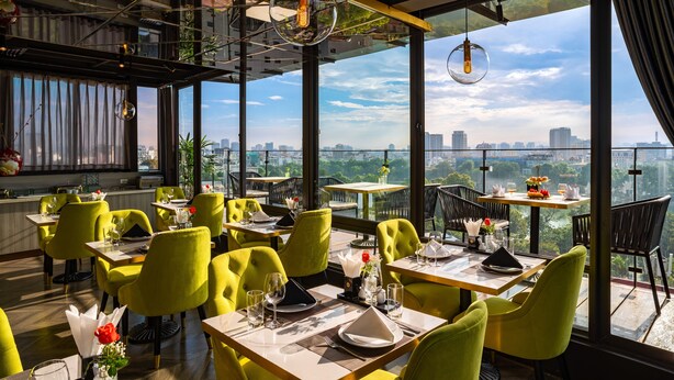 A restaurant with yellow chairs and tables, large windows with a city view, and hanging light fixtures.