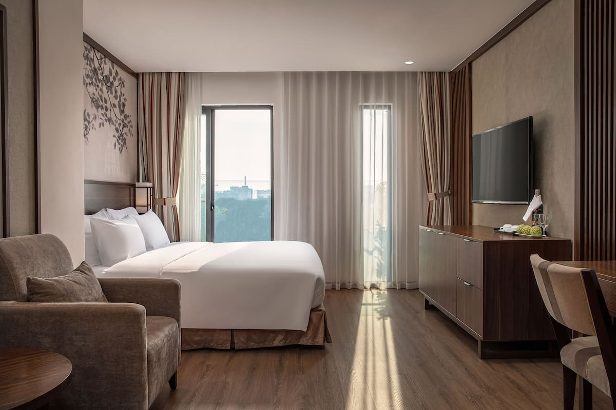 Ein modernes Hotelzimmer mit einem großen Bett, einem Schreibtisch, einem Fernseher und Blick auf die Stadt.