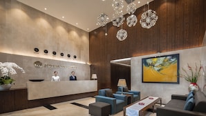 A modern hotel lobby with a reception desk, seating area, and a large painting on the wall.