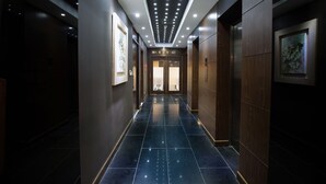 A modern hotel corridor with a dark floor, recessed lighting, and framed artwork on the walls.