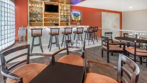 Un espace bar doté de plusieurs tabourets et d’un comptoir, entouré de chaises et de tables en bois.