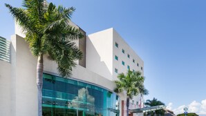 Un hôtel moderne doté d’une façade en verre, de palmiers et d’une structure surmontée d’un toit de chaume.