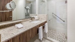 A modern bathroom with a granite countertop, a wooden vanity, a glass shower enclosure, and a large mirror.