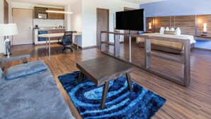 Une chambre d’hôtel moderne équipée d’un canapé, d’une petite table, d’une télévision, d’un lit, d’un bureau et d’une kitchenette.