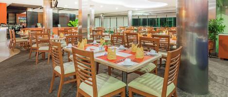 Un restaurante amplio con varias mesas y sillas, que destaca por su diseño moderno con mobiliario de madera y suelo alfombrado.