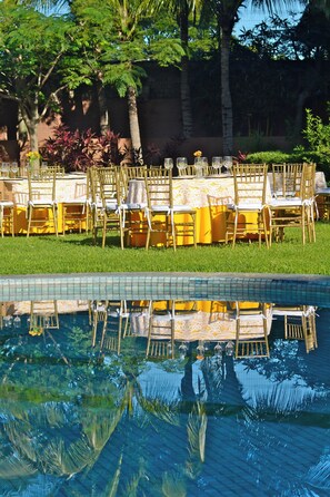 An outdoor dining area with tables and chairs, a pool, and surrounding greenery.