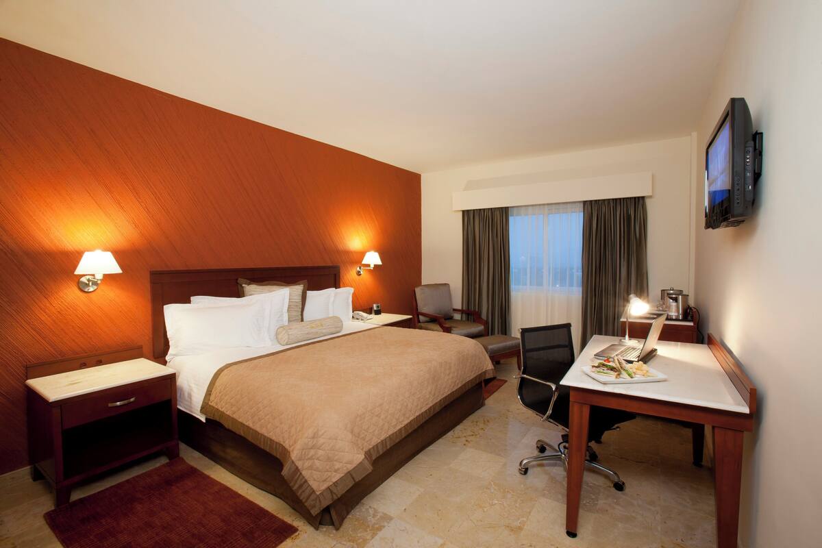 A hotel room with a large bed, a desk with a laptop, a TV, and two bedside lamps.