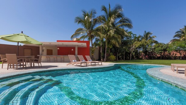 Une piscine dont le fond est décoré de motifs en mosaïque, des chaises longues et, au fond, un bâtiment rouge.