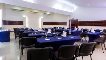 Uma sala de conferência com mesas preparadas para uma reunião, equipada com cadeiras e mesas, e uma porta ao fundo.