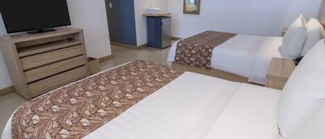 Habitación de hotel con dos camas, un televisor sobre una cómoda de madera, un escritorio pequeño y un espejo en la pared.