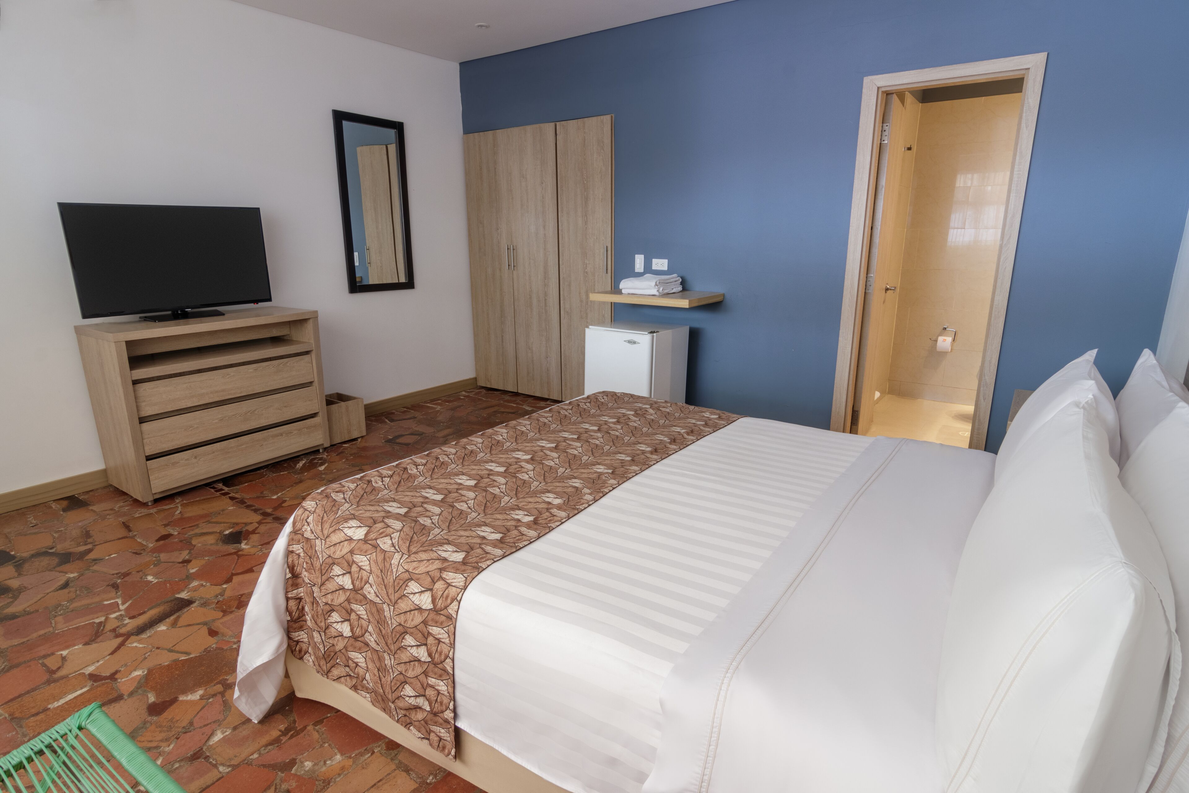 A bedroom with a bed, a TV, a wardrobe, a small fridge, and a door.