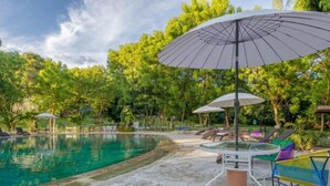 Una piscina con sillas de descanso y sombrillas, rodeada de árboles.