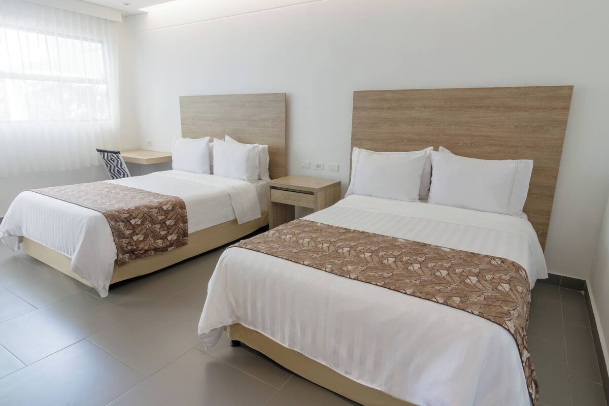 Une chambre d’hôtel avec deux lits, chacun doté d’une tête de lit en bois, de draps blancs et d’un couvre-lit à motifs.