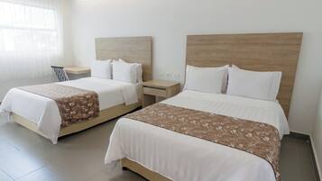Quarto de hotel com duas camas, cada uma com cabeceira de madeira, roupa de cama branca e manta estampada.