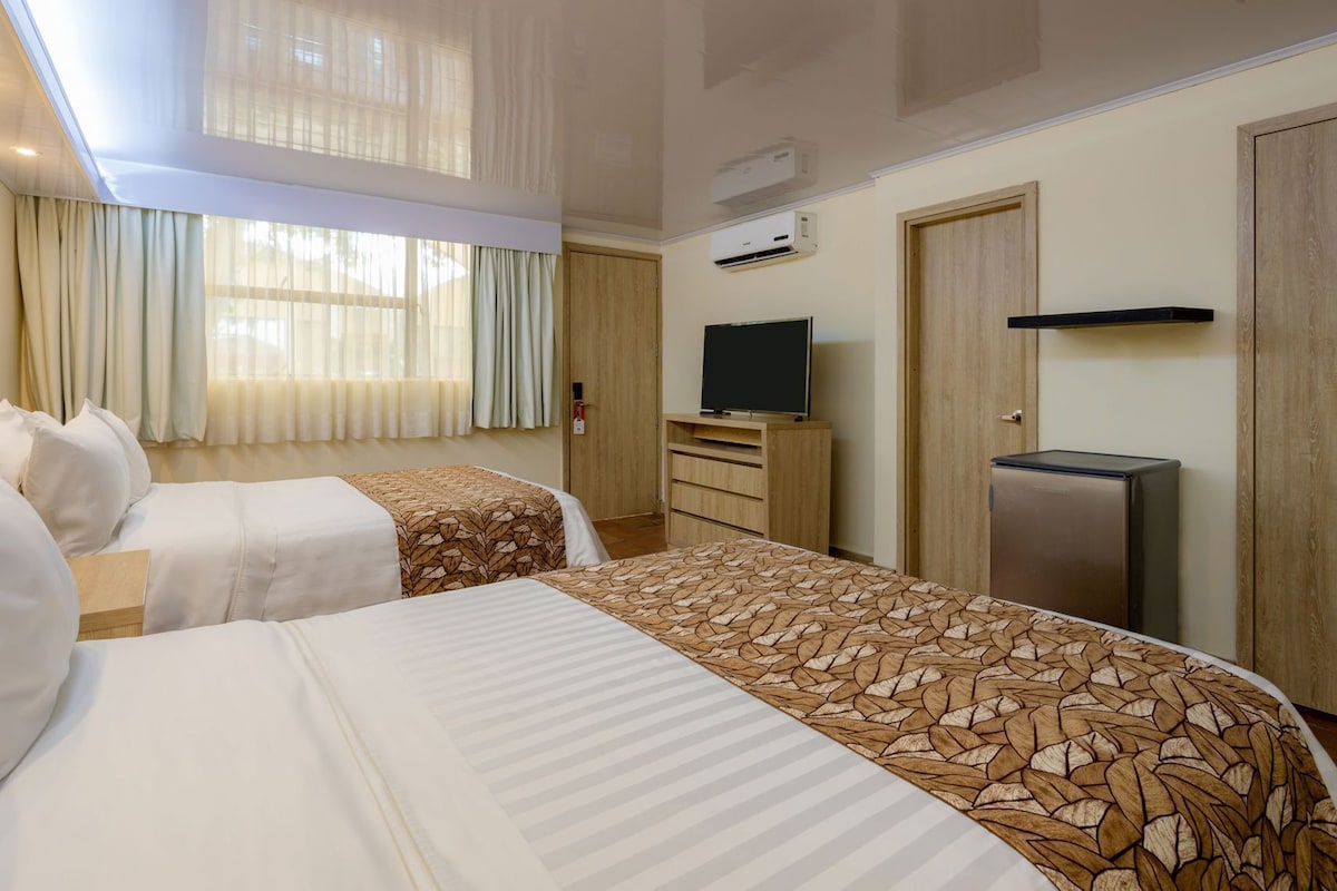 Een hotelkamer met twee bedden, een televisie, een koelkast en een airconditioner.