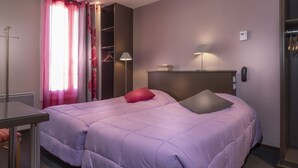 Een hotelkamer met een bed, een bureau, een stoel, een kledingkast en een bedlampje.