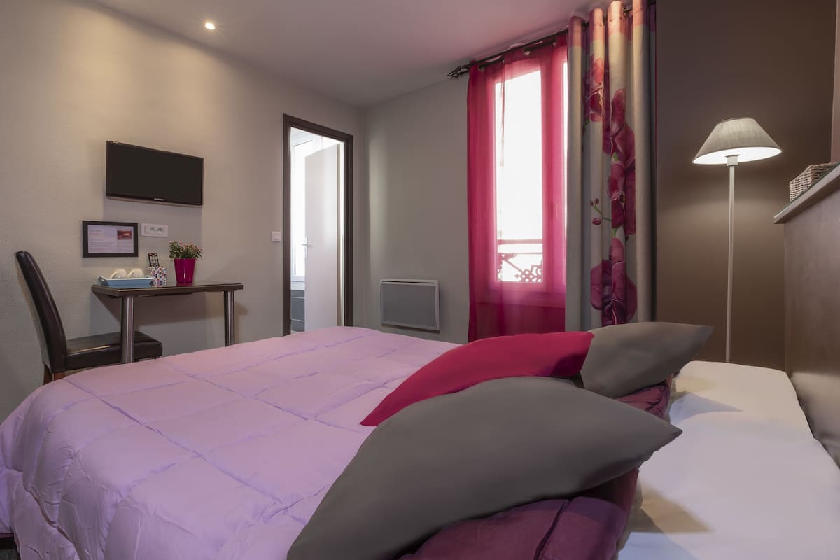 A hotel room with a bed, a desk with a chair, a TV, and a window with curtains.