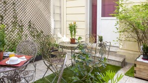 Een terras met metalen stoelen en tafels, omringd door potplanten en een klein gazon.