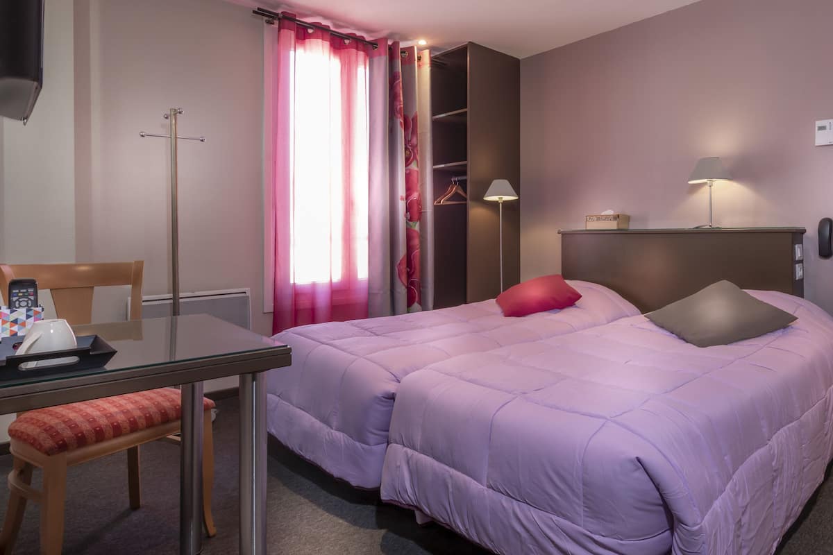 A hotel room with a bed, a desk with a chair, a lamp, and a wardrobe.