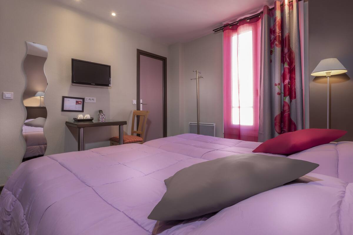 A hotel room with a bed, a desk, a chair, a TV, a lamp, and a window with curtains.