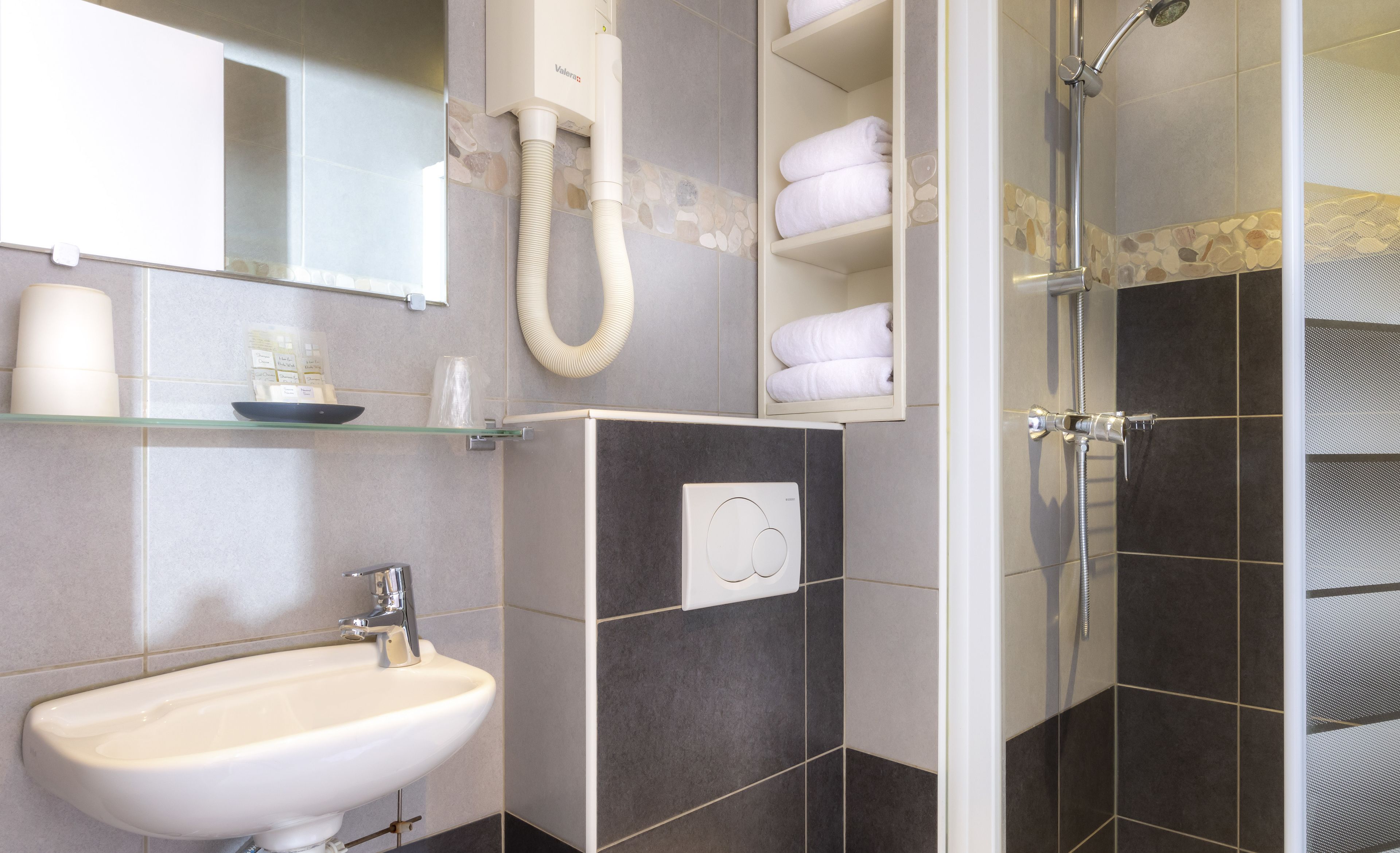 Une salle de bain comprenant un lavabo, un miroir, un porte-serviettes et un espace douche.