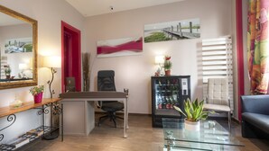 Een moderne woonkamer met een glazen salontafel, een bank, een bureau met een computer, een stoel, een automaat en een grote spiegel.