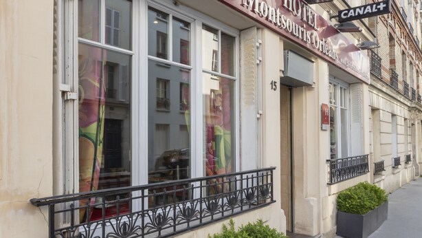 Gevel van een hotel met een contactnummer, een bord dat een locatie aan het kanaal aangeeft, en een balkon met planten.