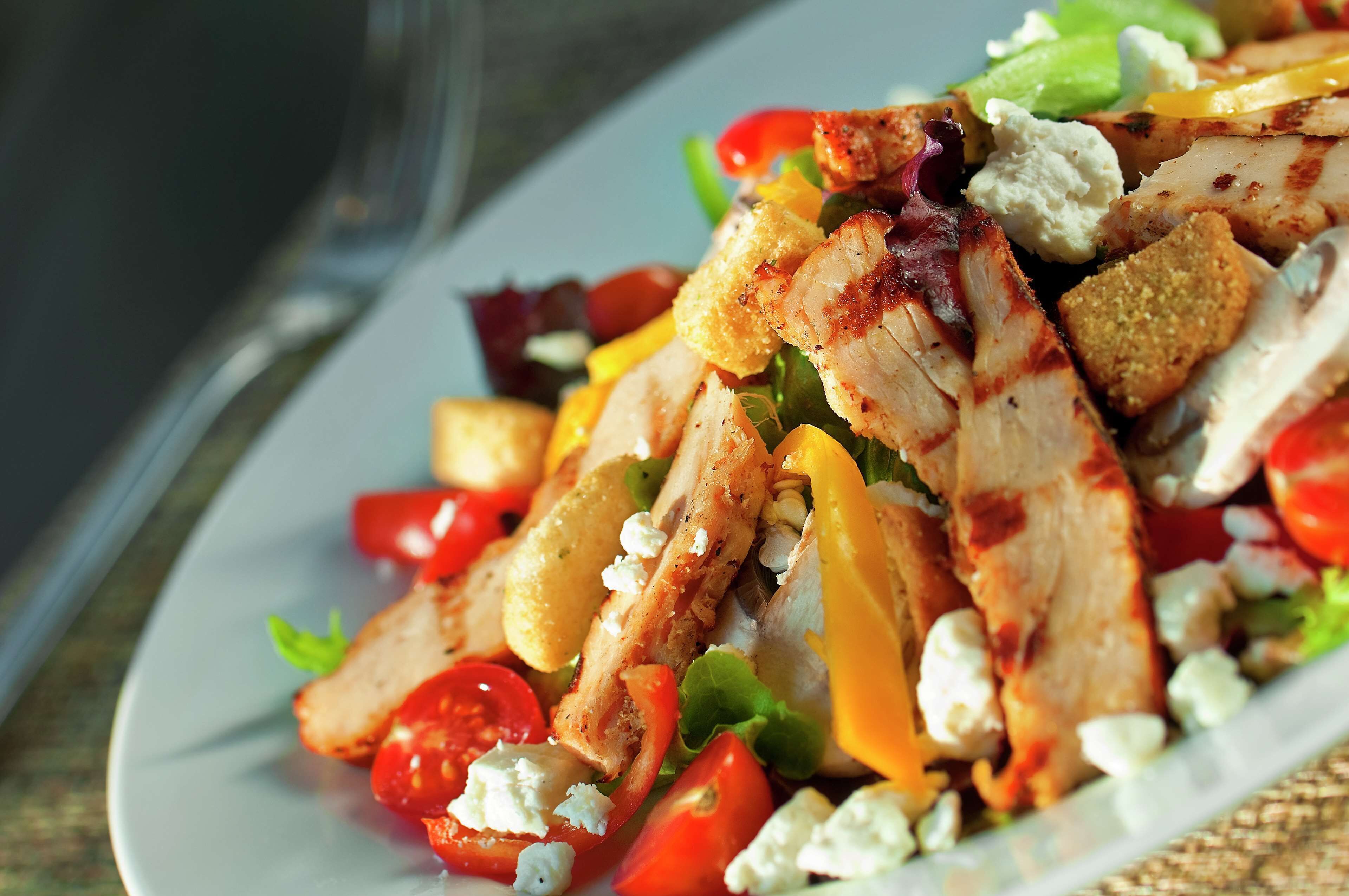 Une assiette de salade de poulet grillé, garnie de tomates, de fromage et de croûtons.