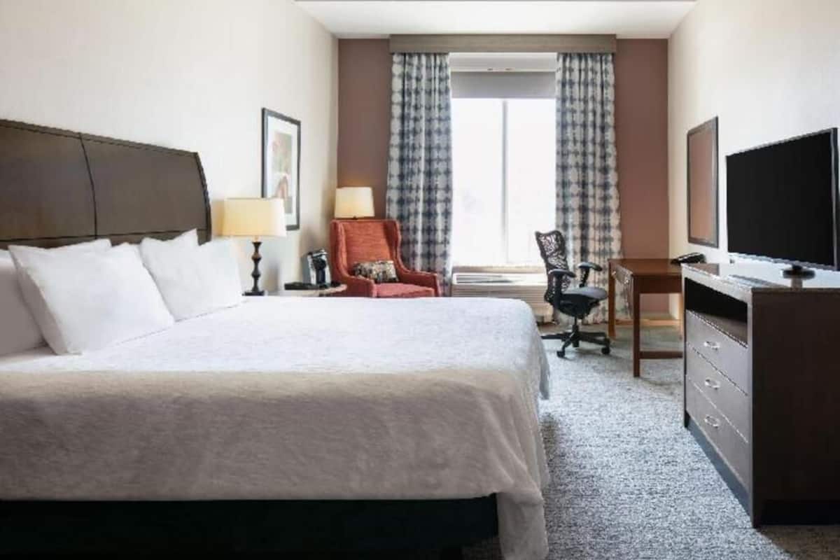 A hotel room with a bed, a desk, a chair, a television, and a window with curtains.