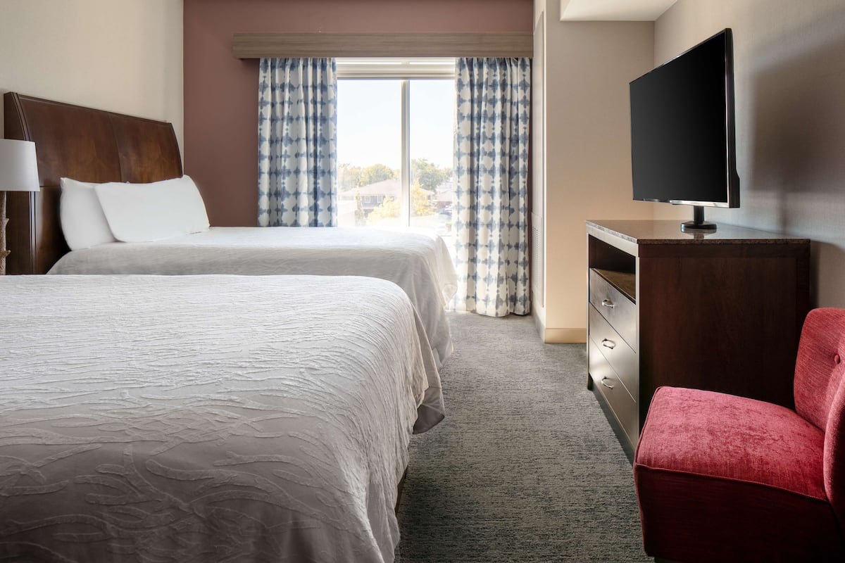 A hotel room with two beds, a TV, a red chair, and a dresser.