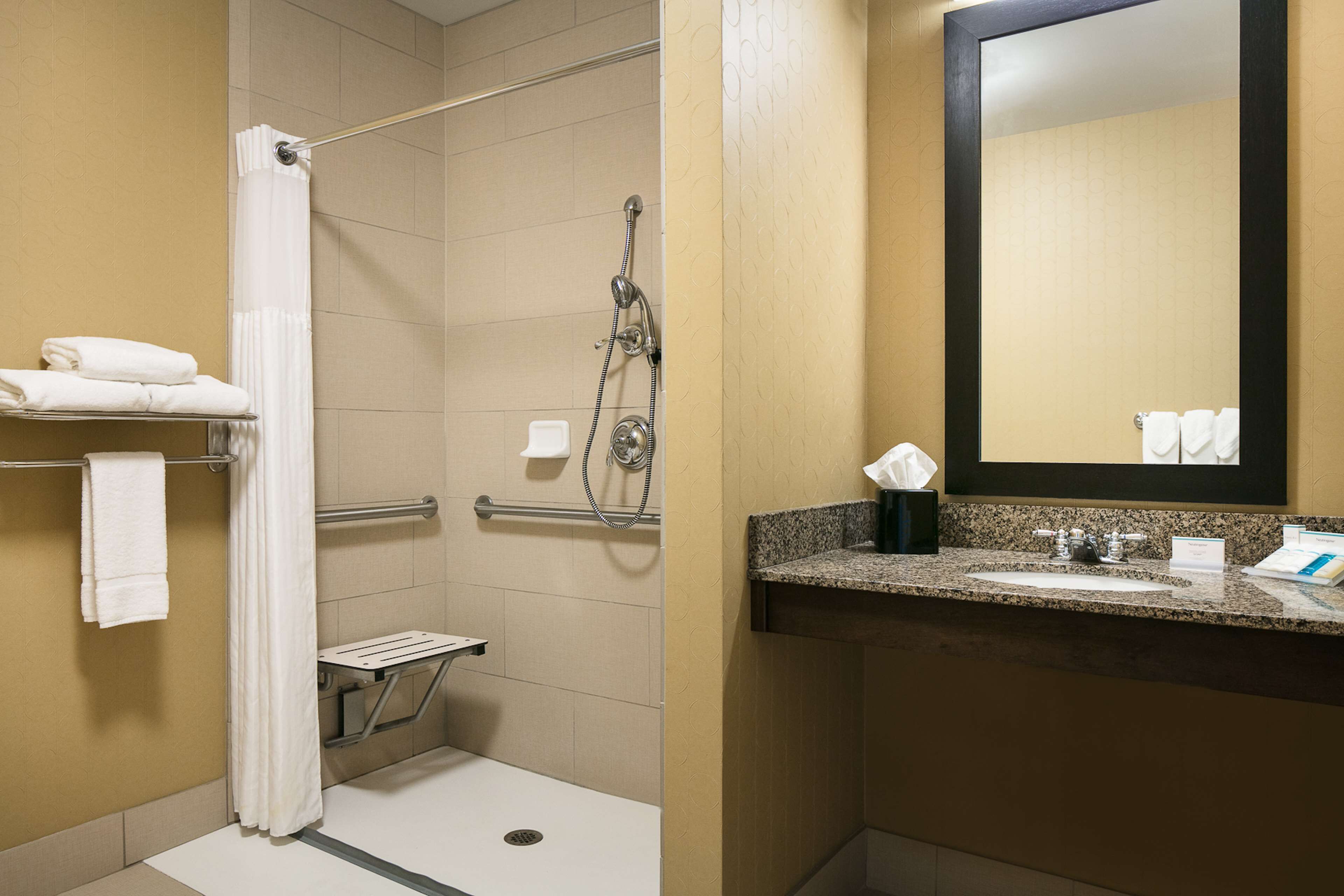 A bathroom with a shower, grab bar, and a sink with a mirror.