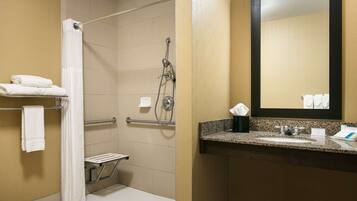 A bathroom with a shower, grab bar, and a sink with a mirror.