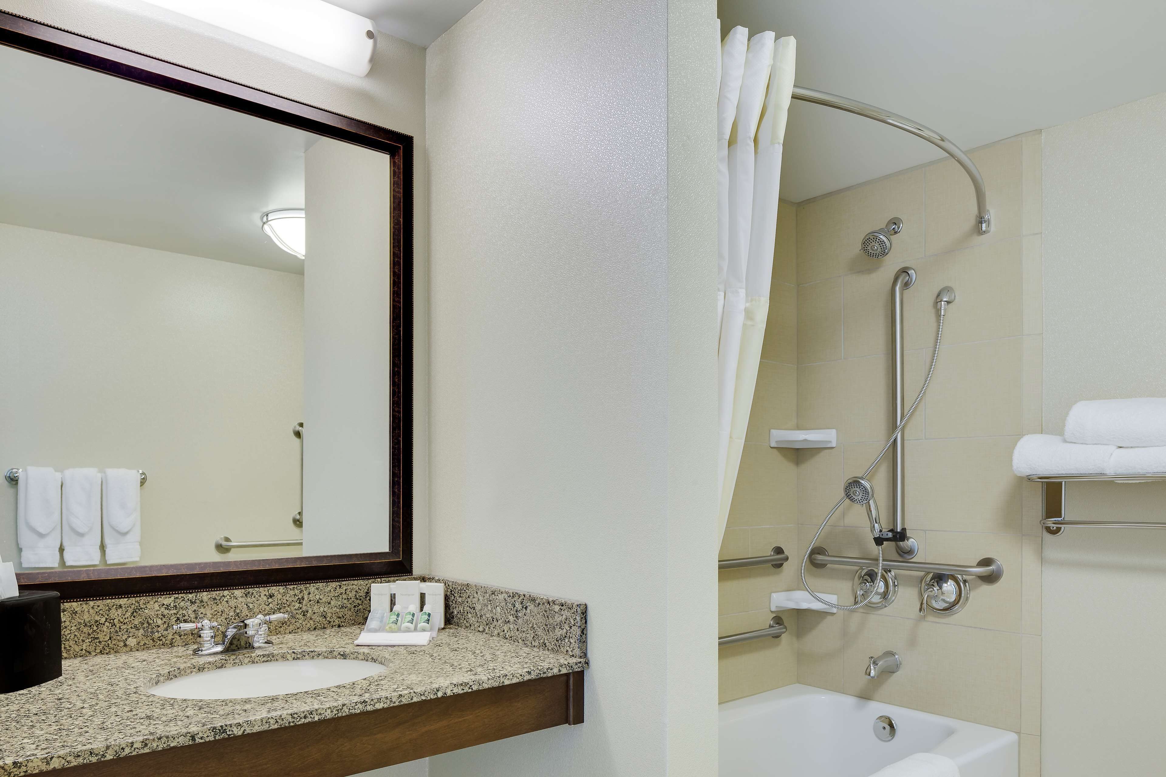 A bathroom with a granite countertop sink, a mirror, a shower with a handheld showerhead, and a bathtub.