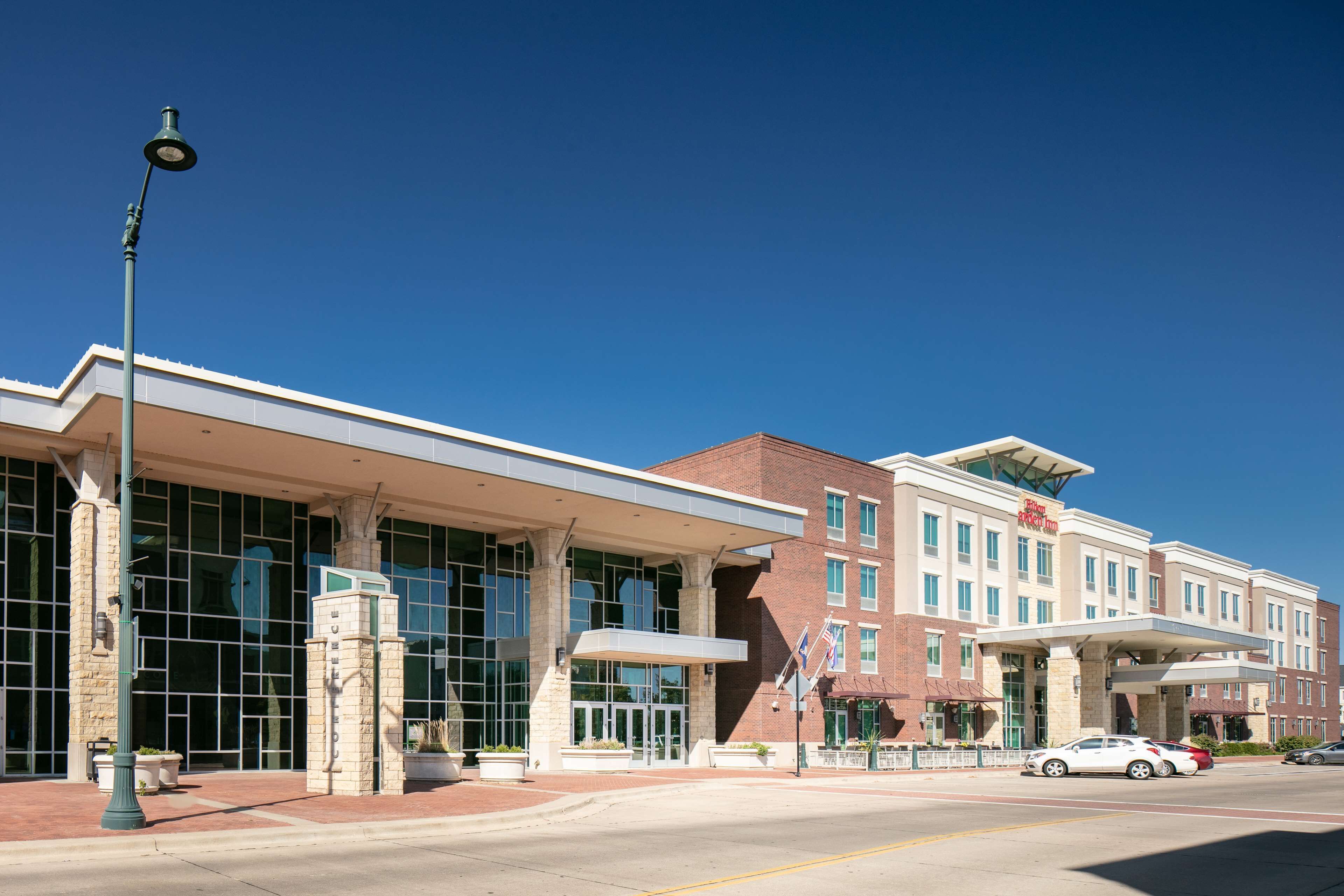 A modern hotel with a glass facade, a covered entrance, and a parking lot.