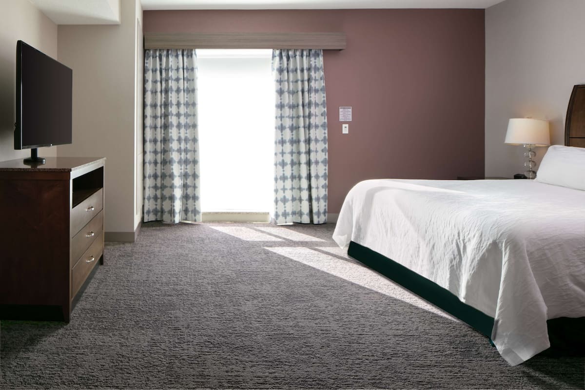 A hotel room with a bed, a TV, a dresser, and a window with curtains.