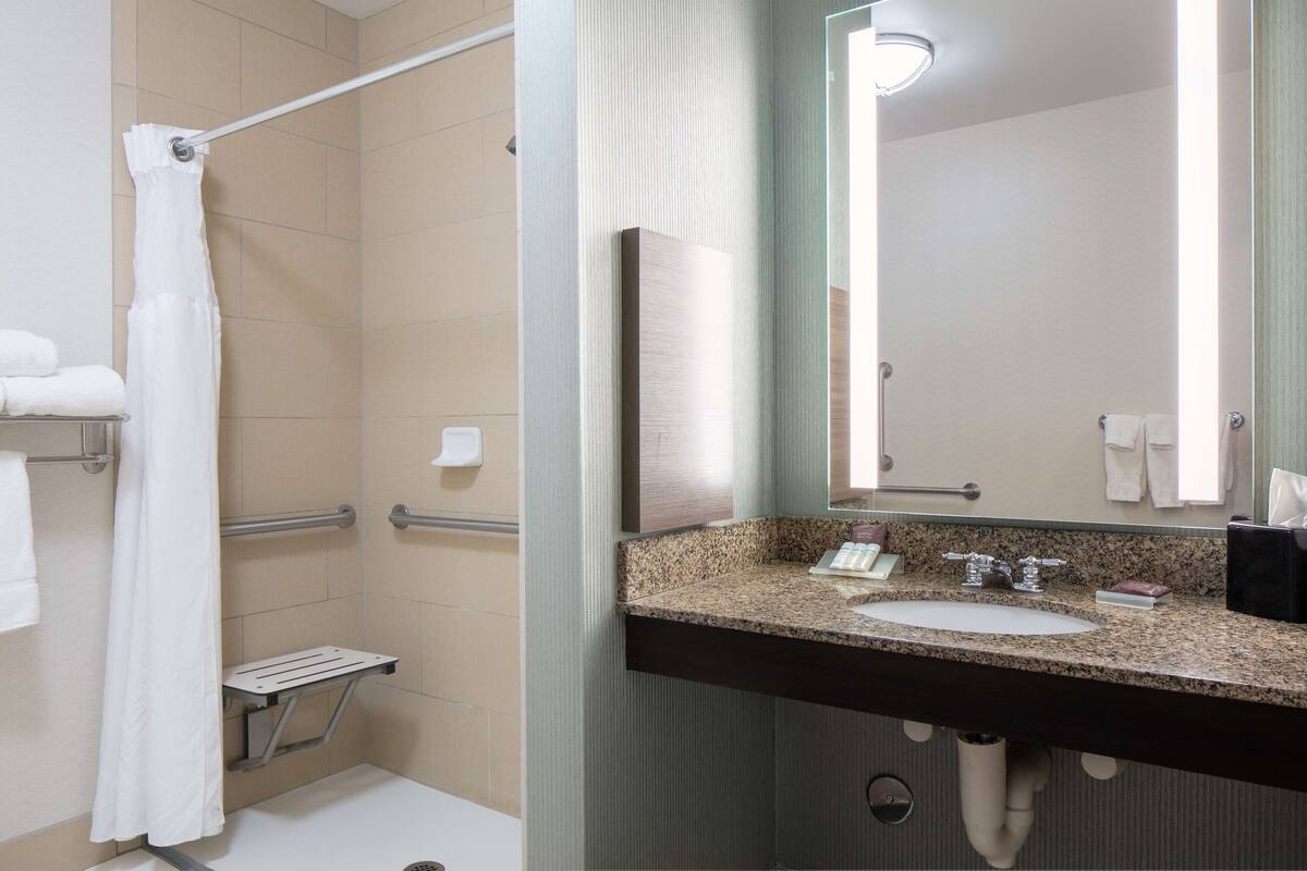 A bathroom with a shower, grab bar, and a sink with a mirror.