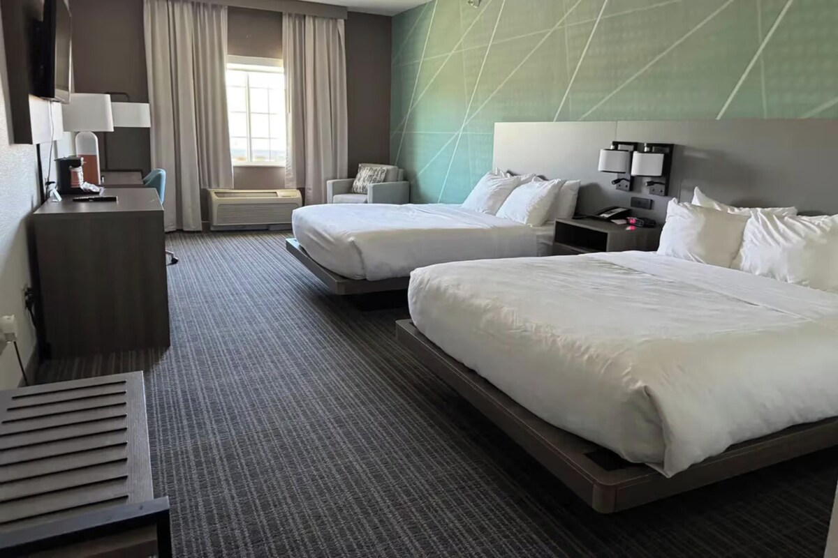 Habitación de hotel con dos camas, un escritorio, una silla, televisión y ventana con cortinas.