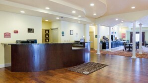 Un hall d’hôtel comprenant un comptoir d’accueil, un revêtement de sol en bois et un espace détente avec des tables et des chaises.