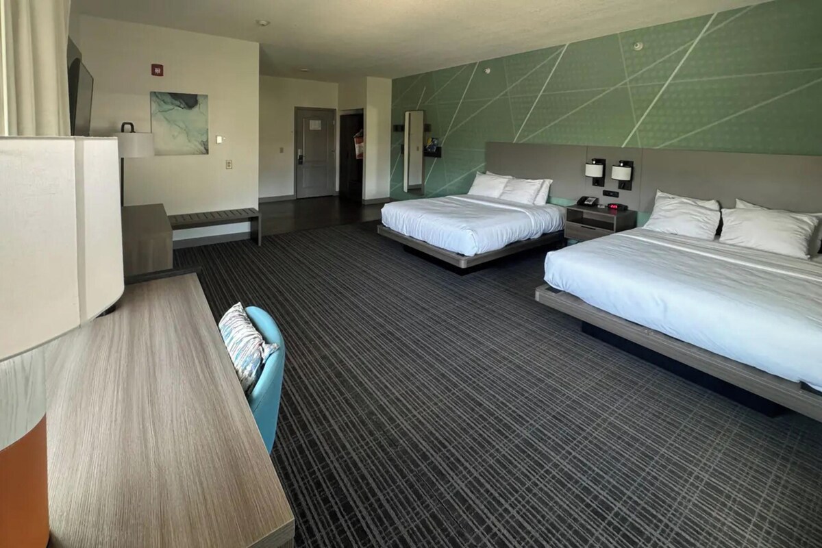 Habitación de hotel con dos camas, un escritorio, una silla, un espejo y una pared verde de acento.