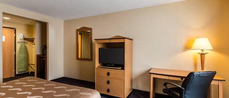 A hotel room with a bed, a desk with a chair, a television, a lamp, and a wardrobe.