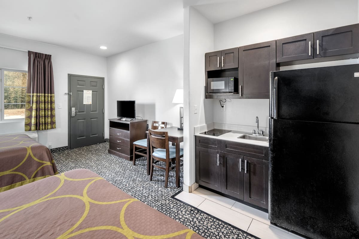 A hotel room with a kitchenette, a desk, a chair, a bed with patterned bedding, and a window with curtains.