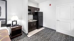 A compact hotel room with a kitchenette, a bed, a bedside table with a lamp, and a framed picture on the wall. - Super 8 by Wyndham Mansfield LA (Mansfield)
