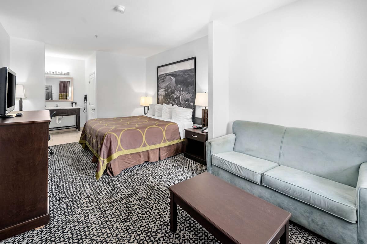 A hotel room with a bed, a sofa, a desk with a computer, a TV, and a large window.