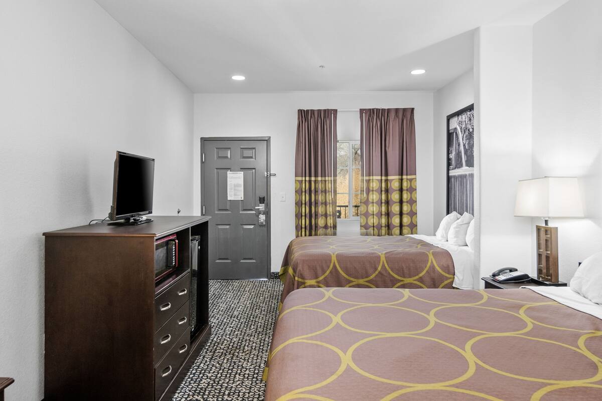 A hotel room with two beds, a TV, a desk, and a lamp.