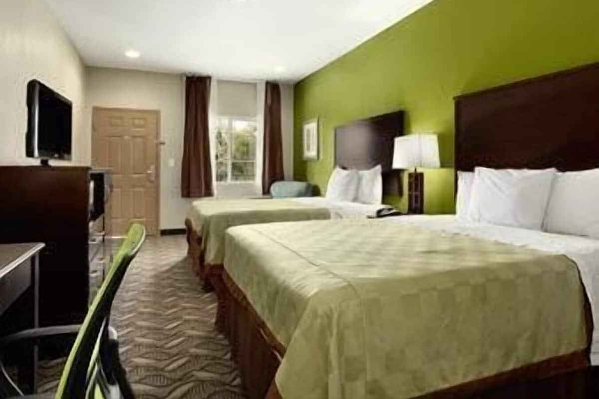 A hotel room with two beds, a desk, a chair, a television, and a window with curtains.